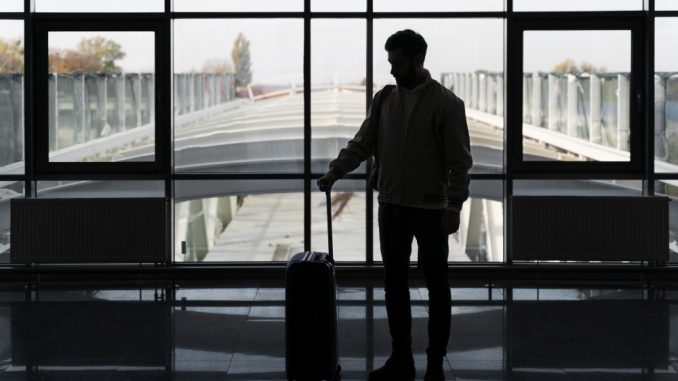 Bărbat cu troler într-un terminal de aeroport, pregătit să își continue călătoria după aterizare
